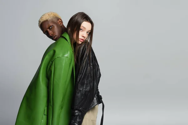 Bionda afro-americana uomo e bruna donna guardando la fotocamera mentre si appoggiano l'uno all'altro isolati sul grigio — Foto stock