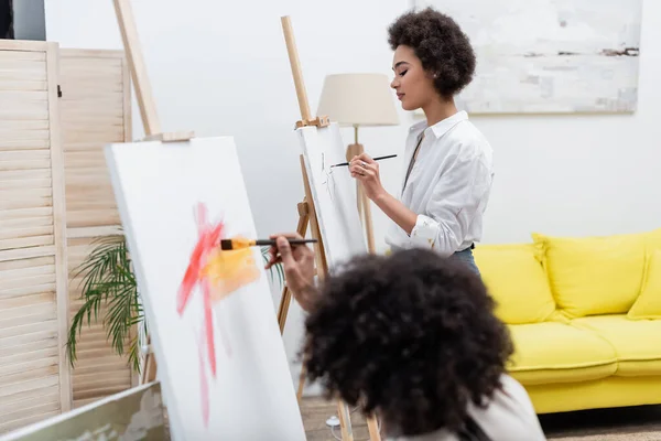 Afro-américaine femme peinture sur toile près petit ami à la maison — Photo de stock