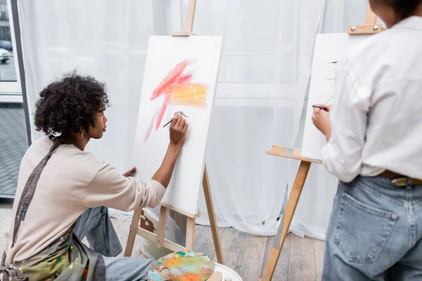 Jeune homme afro-américain peinture sur toile près de petite amie floue à la maison — Photo de stock