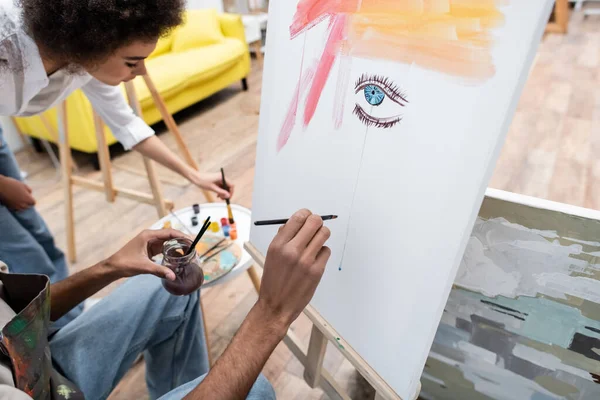 Young african american man drawing on canvas near girlfriend and paints at home — Stock Photo
