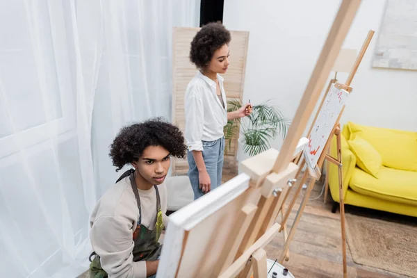Young african american couple looking at canvases on easels at home — Stock Photo