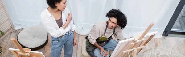 Vista aerea dell'uomo afroamericano che dipinge su tela vicino alla ragazza a casa, banner — Stock Photo