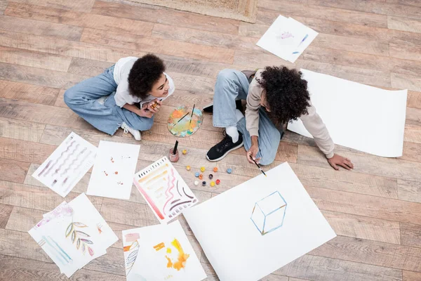 Overhead-Ansicht positiver afrikanisch-amerikanischer Paarmalerei auf dem Boden in der Nähe von Palette und Farben zu Hause — Stockfoto