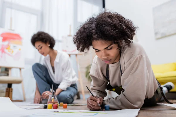 Giovane uomo africano americano pittura su carta sfocata vicino fidanzata a casa — Foto stock