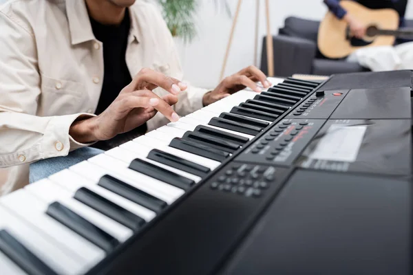 Vista recortada del hombre afroamericano tocando sintetizador cerca de mujer borrosa con guitarra acústica en casa — Stock Photo