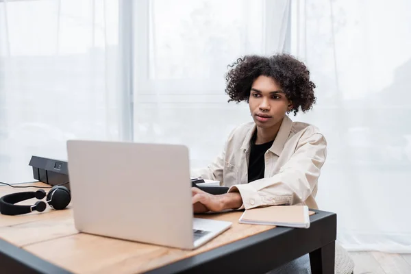 Junger Afroamerikaner benutzt Laptop in der Nähe des Synthesizers zu Hause — Stockfoto