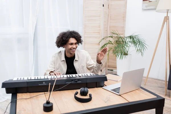 Smiling african american man having video call on laptop near synthesizer at home — Stock Photo