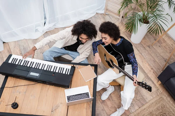 Vue aérienne du couple afro-américain jouant des instruments de musique près d'un ordinateur portable à la maison — Photo de stock