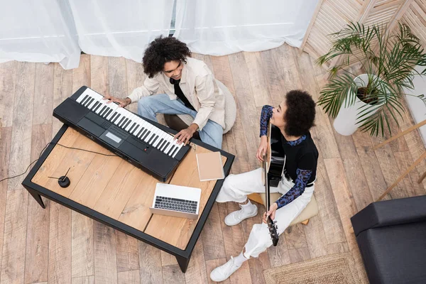 Vista aérea de la sonriente pareja afroamericana tocando instrumentos musicales cerca de la computadora portátil en casa - foto de stock