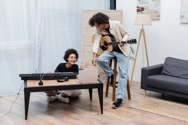 Couple afro-américain positif avec instruments de musique ayant appel vidéo sur ordinateur portable à la maison — Photo de stock