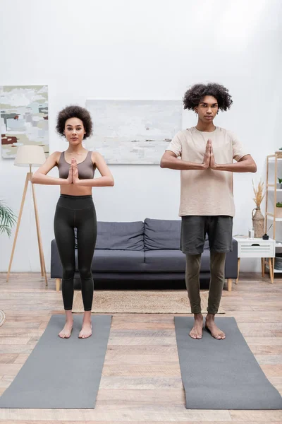 Joven pareja afroamericana de pie en yoga posan sobre alfombras en casa - foto de stock