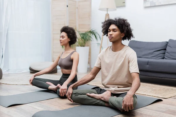 Coppia afroamericana meditando su stuoie yoga in soggiorno — Foto stock