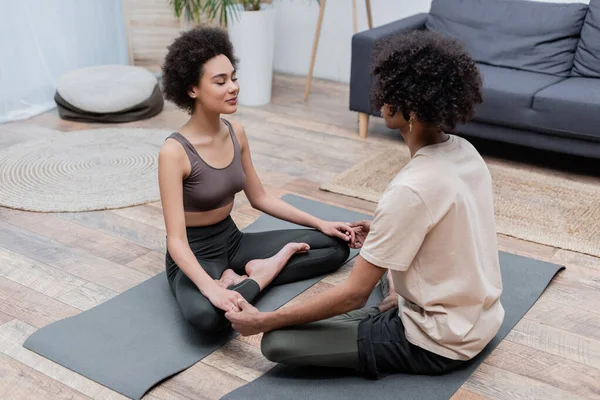 African american woman holding hands of boyfriend while meditating at home — Stock Photo