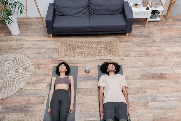 Vista superior do casal afro-americano deitado em tapetes de ioga perto de pau de incenso em casa — Fotografia de Stock