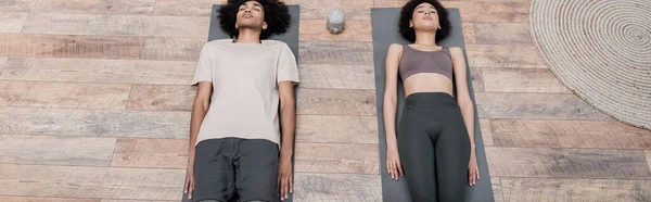 Vue du dessus du couple afro-américain allongé sur des tapis de yoga à la maison, bannière — Photo de stock