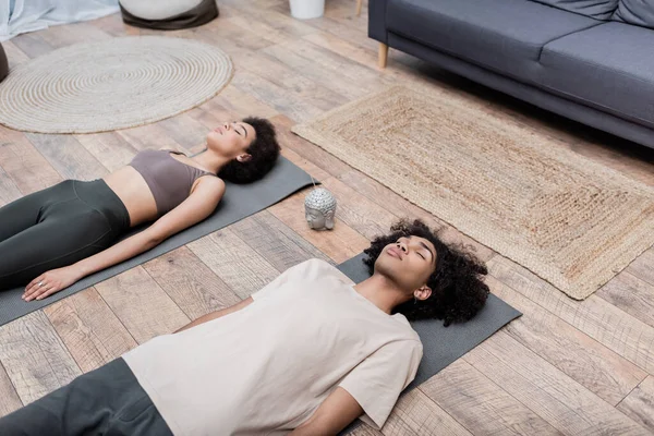 Hochwinkelaufnahme eines afrikanisch-amerikanischen Mannes, der in der Nähe von Freundin und Räucherstäbchen auf Yogamatte liegt — Stockfoto