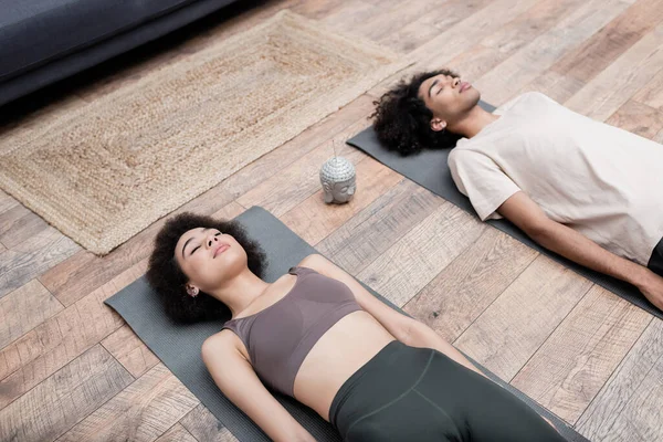 Vista de ángulo alto de la mujer afroamericana meditando cerca de palo de incienso y novio en casa - foto de stock