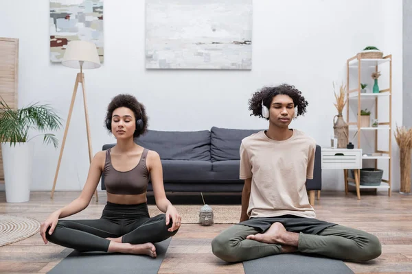 Young african american couple in headphones meditating at home — Stock Photo