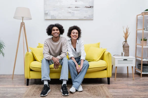 Positiva pareja afroamericana sonriendo a la cámara en el sofá en casa - foto de stock