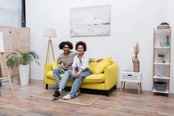 Positivo casal afro-americano sorrindo no sofá perto cavalete em casa — Fotografia de Stock