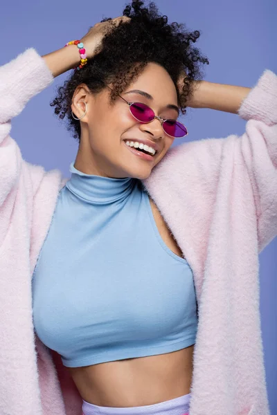 Усміхнена афроамериканська жінка в стильних сонцезахисних окулярах ізольована на фіолетовому — стокове фото
