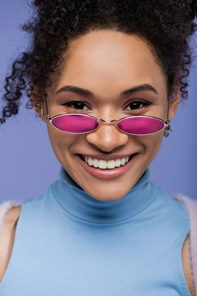 Крупным планом счастливая африканская женщина в стильных солнцезащитных очках, изолированных на фиолетовом фоне — стоковое фото