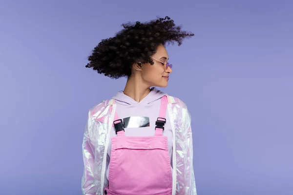 Femme afro-américaine souriante en lunettes de soleil roses secouant la tête isolé sur violet — Photo de stock