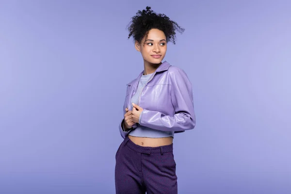 Mujer joven afroamericana en chaqueta de cuero mirando hacia otro lado aislado en púrpura - foto de stock