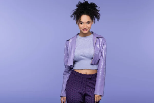 Cheerful and trendy african american woman in leather jacket isolated on purple — Stock Photo