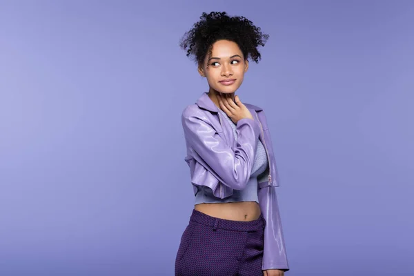 Femme afro-américaine à la mode en veste en cuir regardant loin isolé sur violet — Photo de stock