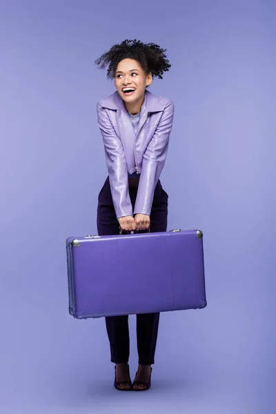 Piena lunghezza della donna afro-americana stupita che tiene la valigia su viola — Foto stock