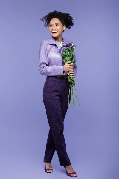 Comprimento total de feliz jovem afro-americana segurando buquê de flores em roxo — Fotografia de Stock