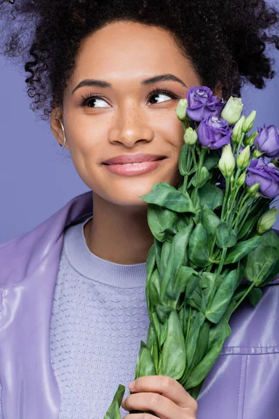 Rêveuse jeune femme afro-américaine tenant bouquet de fleurs violettes isolées sur violet — Photo de stock