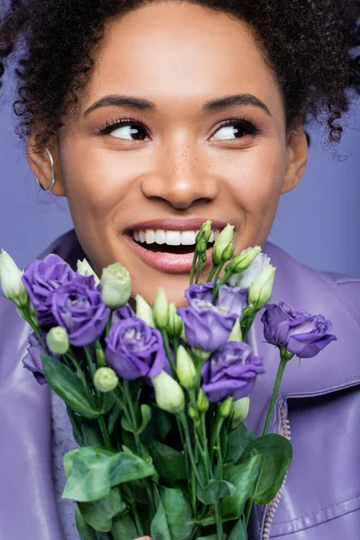 Positive jeune femme afro-américaine près de fleurs violettes isolées sur violet — Photo de stock