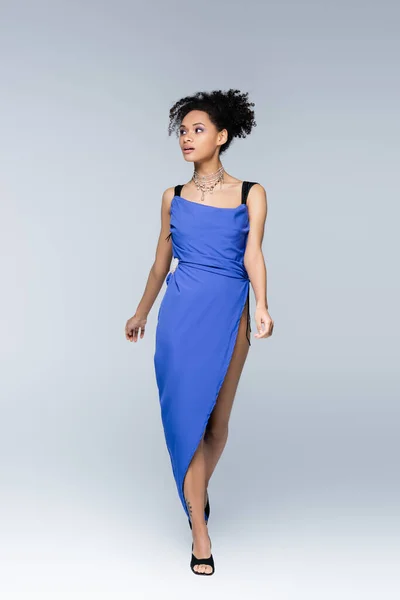 Full length of curly african american woman in bright blue dress walking on grey — Stock Photo