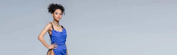 Elegant african american woman in bright blue dress posing with hand on hip isolated on grey, banner — Stock Photo