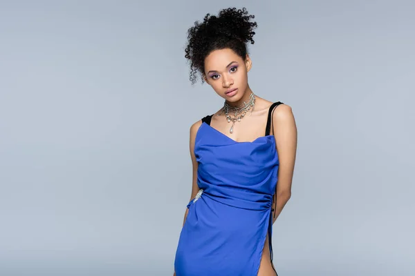 Curly african american woman in bright blue dress looking at camera while posing isolated on grey — Stock Photo