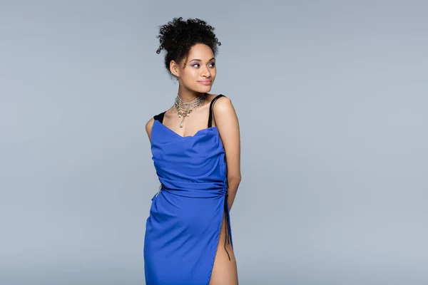 Smiling african american woman in bright blue dress looking away while posing isolated on grey — Stock Photo