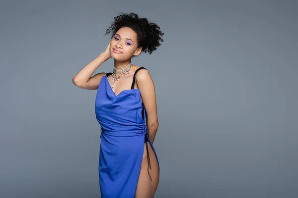 Pleased african american woman in bright blue dress looking at camera while posing isolated on grey — Stock Photo