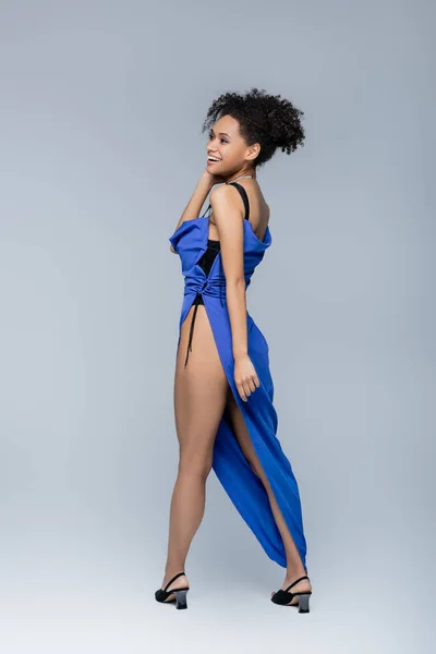 Comprimento total de modelo americano africano alegre em vestido azul brilhante posando em cinza — Fotografia de Stock