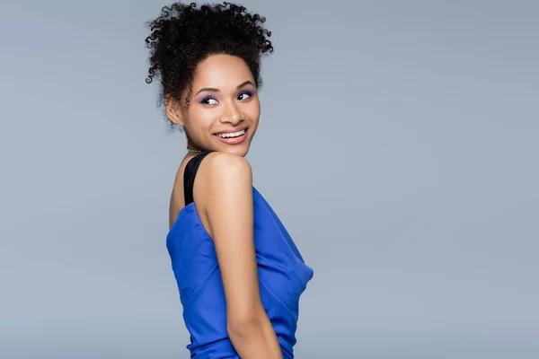 Joyeuse femme afro-américaine en robe glissante brillante regardant loin tout en posant isolé sur gris — Stock Photo