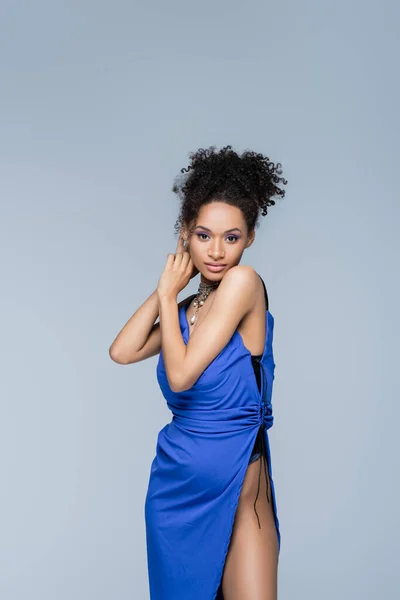 African american woman in bright blue slip dress looking at camera while posing isolated on grey — Stock Photo