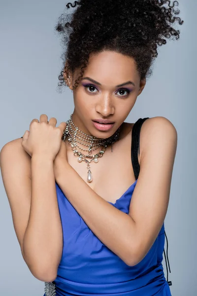 Curly african american woman in dress looking at camera while posing isolated on grey — Stock Photo