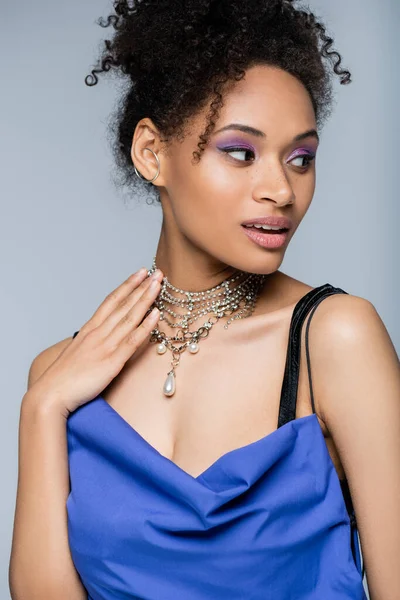 Curly african american woman with purple eye shadow looking away isolated on grey — Stock Photo