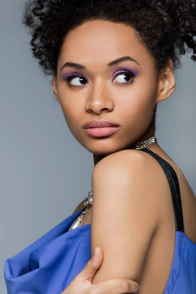 Curly african american woman with lilac eye shadow isolated on grey — Stock Photo