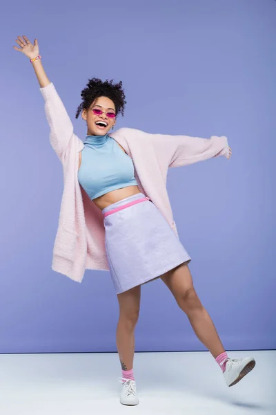 Full length of cheerful african american woman with tattoo and outstretched hands on purple — Stock Photo