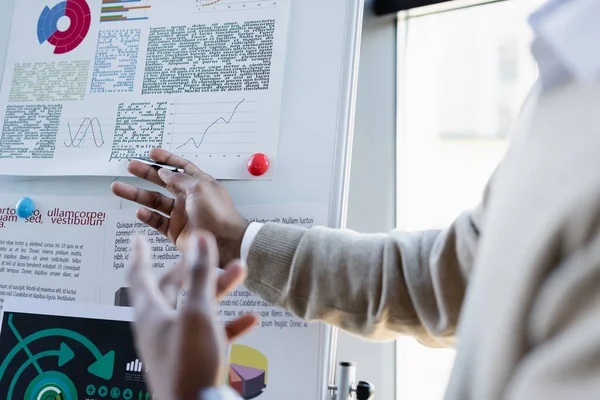 Cropped view of african american man showing infographics on flip chart in office — Stock Photo