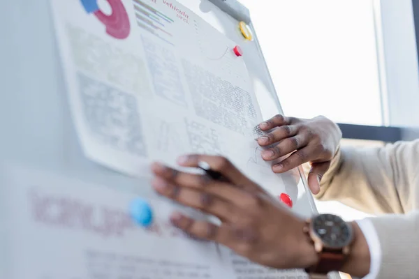 Ausgeschnittene Ansicht eines afrikanisch-amerikanischen Mannes mit Stift in der Nähe von Infografiken auf Flipchart — Stockfoto