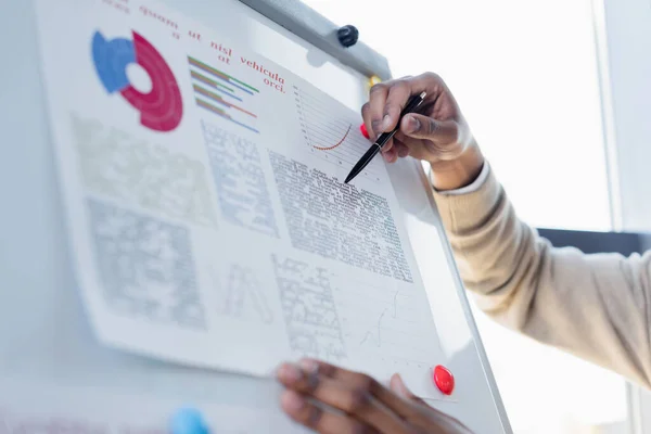 Partial view of african american man pointing with pen at infographics on flip chart — Stock Photo