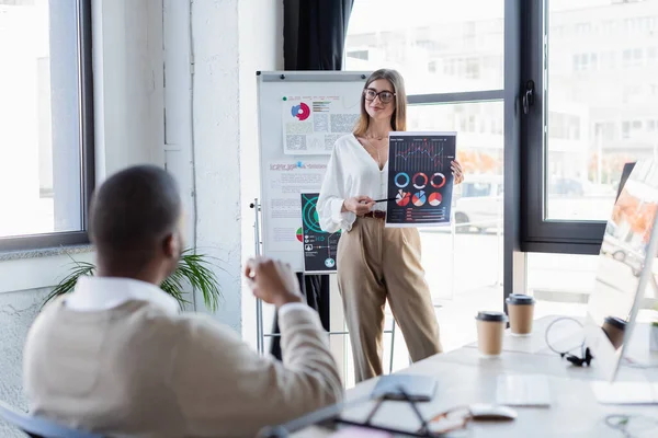 Lächelnde Geschäftsfrau mit Brille zeigt Afrikanern im Büro Infografiken — Stockfoto